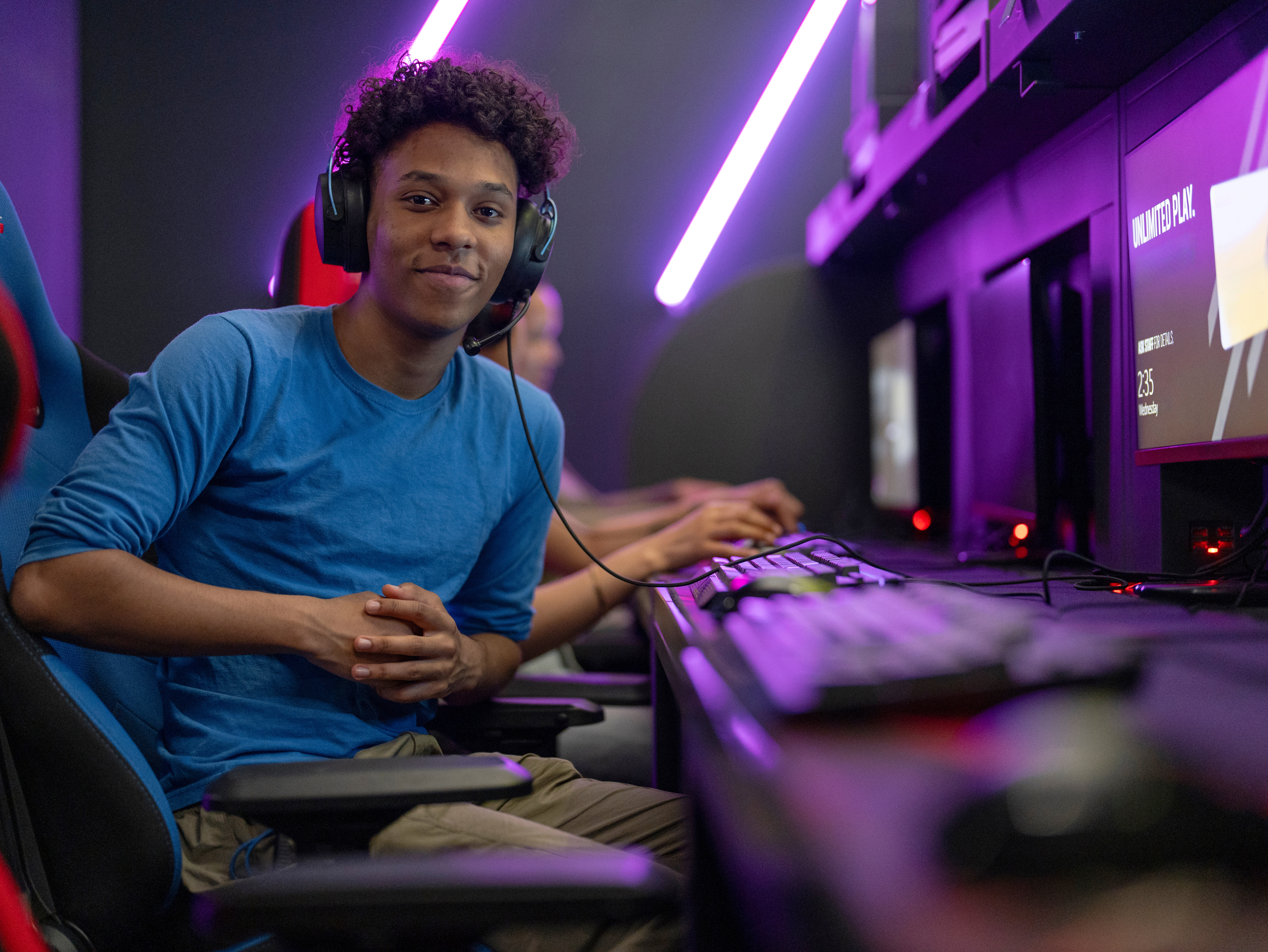 Ein junger Mann mit Kopfhörern sitzt an einem Computerarbeitsplatz in einem Gaming-Raum, bereit zum Spielen.