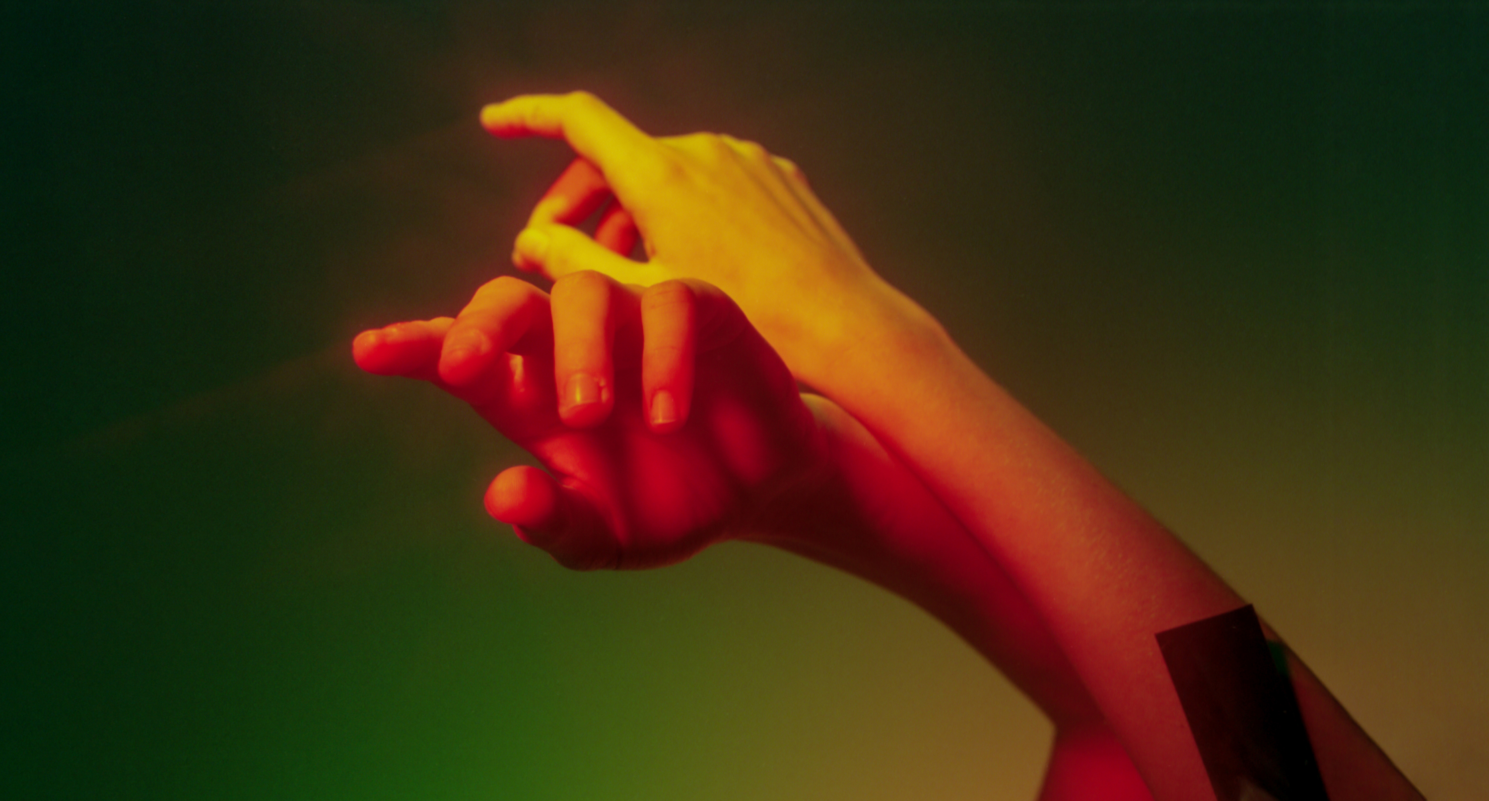 Hands in various skin tones touching and intertwining. The hands are set against a soft, multicolored background that includes shades of green and yellow.