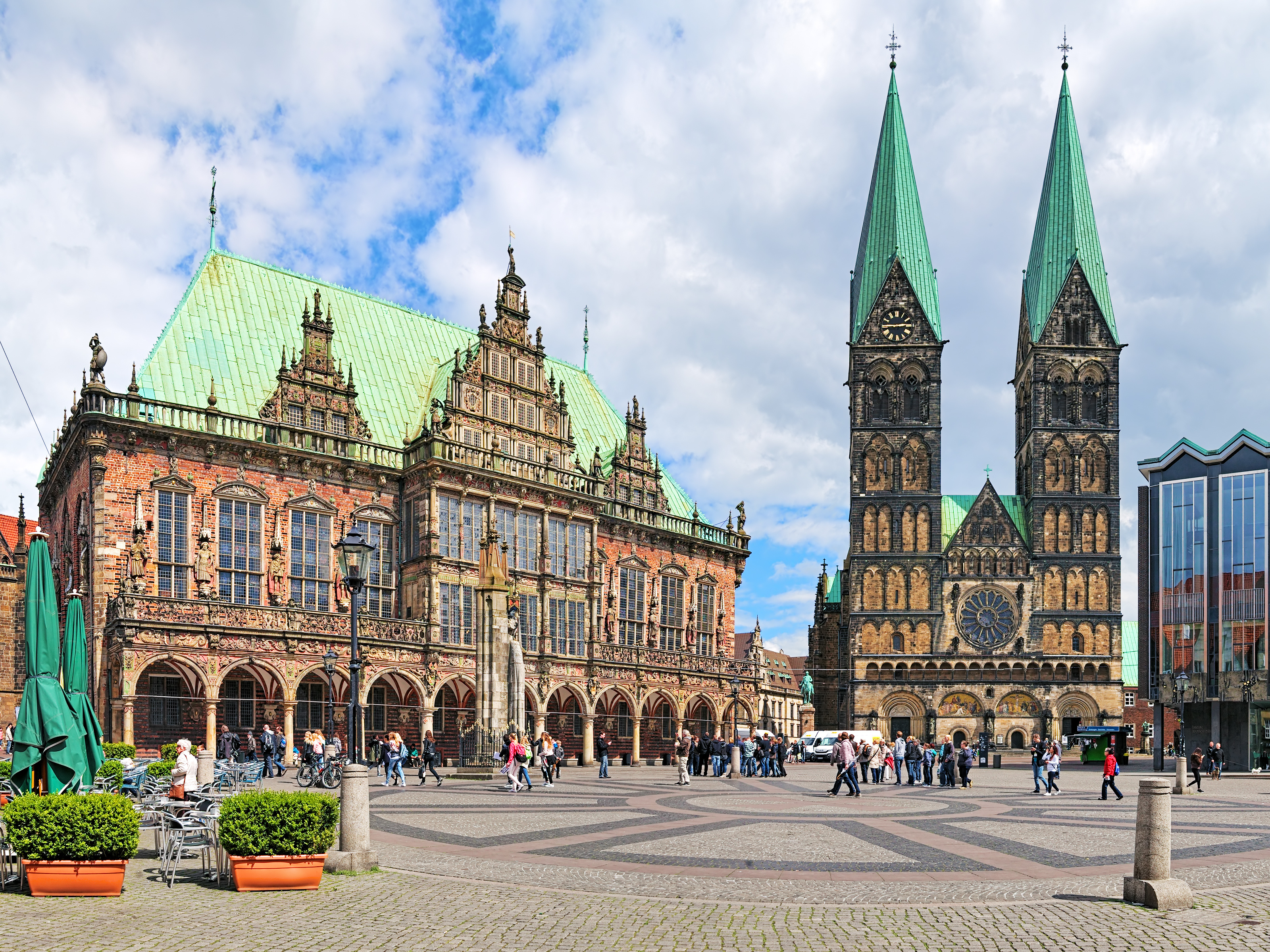 Der Marktplatz in Bremen mit dem historischen Rathaus und den beiden Türmen der St. Petri-Dom. Viele Menschen schlendern umher, während Wolken den Himmel bedecken.