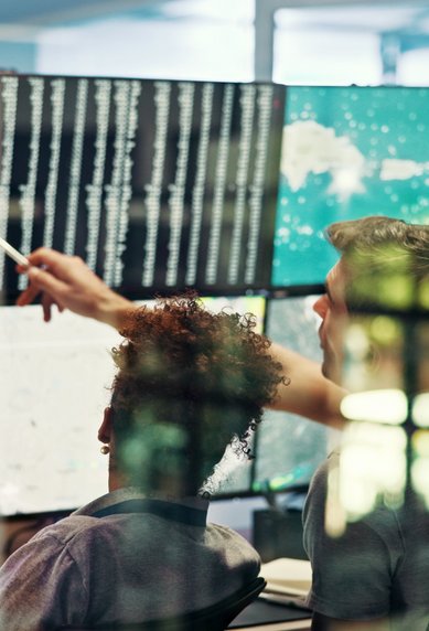 Two people are looking at several computer screens displaying technical data and graphics while they work together on a project.