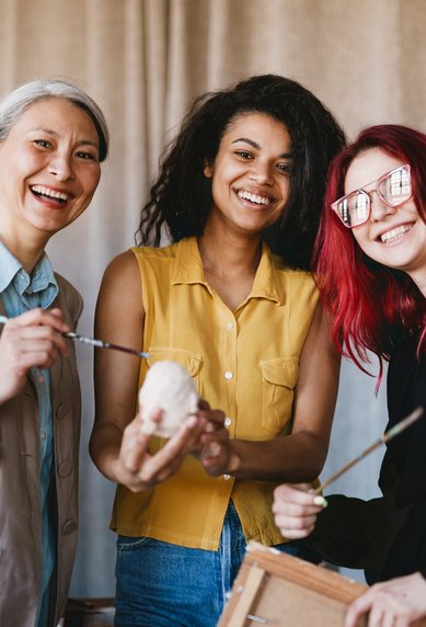 Vier Personen lächeln und halten Malutensilien in einem kreativen Raum. Sie zeigen eine Skulptur und scheinen an einem Kunstprojekt zu arbeiten.