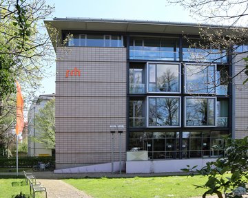 Modern building with large windows and the 'srh' logo on the facade, surrounded by trees and a green area.