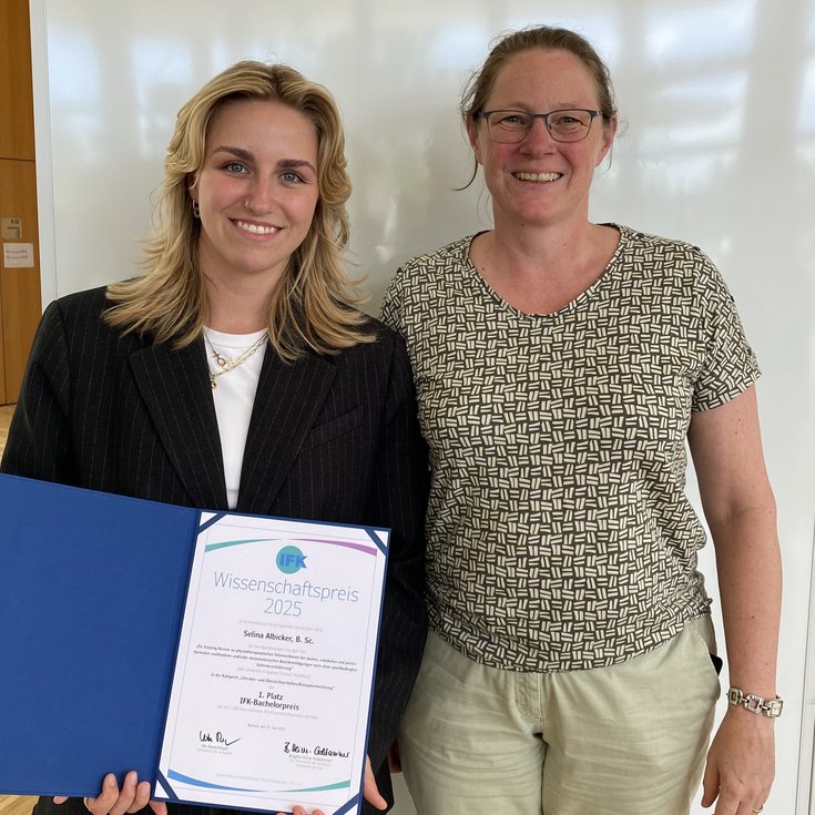 Zwei Frauen stehen nebeneinander, eine hält ein Zertifikat für den Wissenschaftspreis 2025 in der Hand. Beide lächeln in die Kamera.