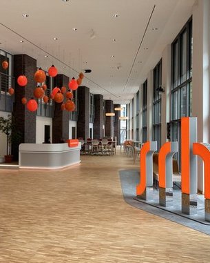 A modern reception area with wooden flooring, large windows, and a staircase. Red lanterns hang from the ceiling, while orange accents highlight the design.