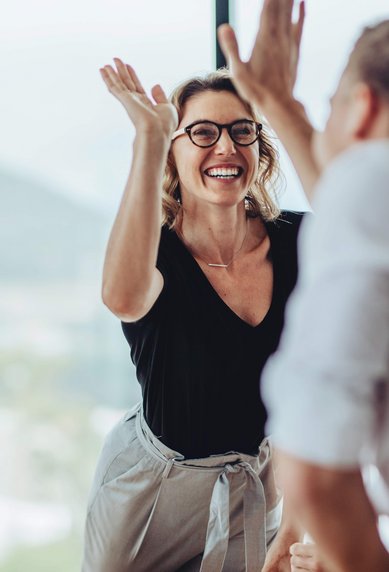 Eine Gruppe von Menschen in einem modernen Büro, wobei eine Frau mit Brille begeistert mit den Händen gestikuliert.