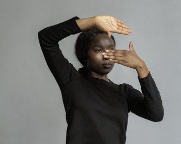 A person in a black top is holding one hand over their face and pointing forward with the other hand.