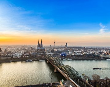 Blick auf Köln mit dem Kölner Dom, der Hohenzollernbrücke und dem Rhein bei Sonnenuntergang.