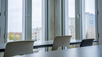 A modern space with large windows overlooking an urban landscape. In the foreground, tables and chairs are set up, ready for a meeting or a class.