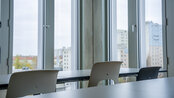 A modern space with large windows overlooking an urban landscape. In the foreground, tables and chairs are set up, ready for a meeting or a class.