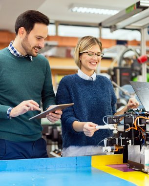 Zwei Personen in einem Labor arbeiten an einem technischen Gerät, während einer ein Tablet hält und der andere das Gerät inspiziert.
