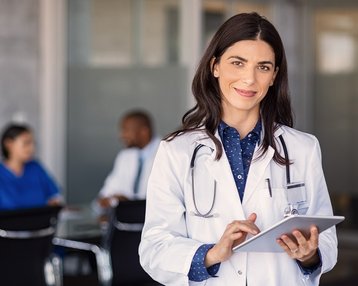 Doctor smiles at the camera with a tablet in hand.