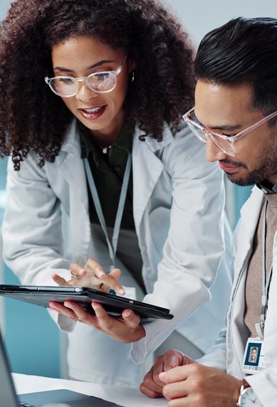 Two scientists in lab coats are working together on a laptop and a tablet in a modern laboratory.
