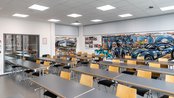 Ein moderner Klassenraum mit mehreren Tischen und Stühlen, dekoriert mit Graffiti-Kunst und Bildern von Rennwagen.