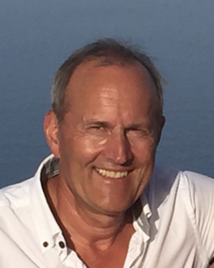 A man with short gray hair and a white shirt smiles at the camera against a blue background.