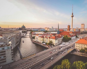 View of the Berlin skyline featuring the TV Tower, historic buildings, and the Spree River. The scene showcases a blend of modern and classical architecture, surrounded by water and traffic.