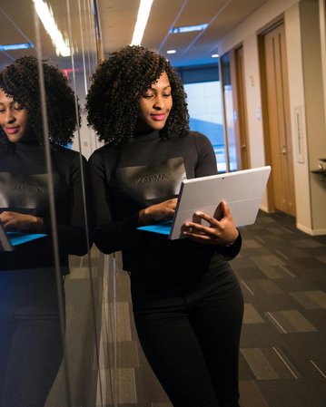Kategorie Data Science studieren Studium SRH University Eine Frau mit lockigem Haar steht in einem modernen Büro und betrachtet ein Tablet. Sie trägt ein schwarzes Oberteil und steht vor einer reflektierenden Wand. Im Hintergrund sind Server zu sehen.