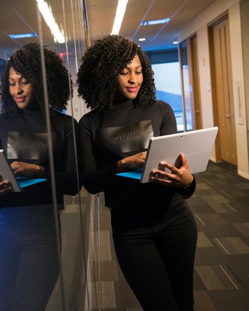 Kategorie Data Science studieren Studium SRH University Eine Frau mit lockigem Haar steht in einem modernen Büro und betrachtet ein Tablet. Sie trägt ein schwarzes Oberteil und steht vor einer reflektierenden Wand. Im Hintergrund sind Server zu sehen.