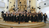 A group of graduates in academic attire throwing their hats in the air, set against an ornate backdrop in a hall.