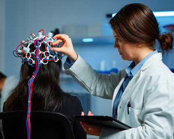 Eine Fachkraft befestigt Elektroden an der Kopfhaut einer Person für eine neurologische Untersuchung in einem Labor.