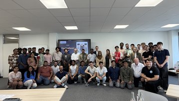 A group of about 40 people stands together in a modern office, smiling and posing for a group photo.