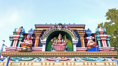 Bunte Tempelarchitektur mit Skulpturen von Gottheiten, darunter eine zentrale Figur mit mehreren Armen und symbolischen Objekten.