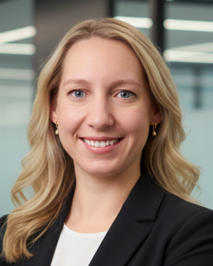 Eine blonde Frau mit langen Haaren trägt einen schwarzen Blazer und lächelt in die Kamera, vor einem modernen Bürohintergrund.