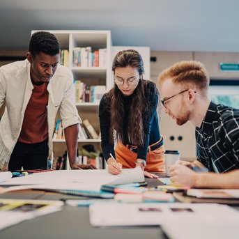 Three people are working at a table, surrounded by notes and materials. They are discussing and analyzing documents in a modern office.