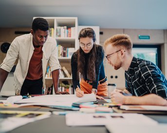 Three people are working at a table, surrounded by notes and materials. They are discussing and analyzing documents in a modern office.