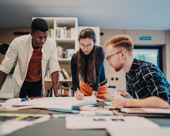 Drei Personen arbeiten an einem Tisch, umgeben von Notizen und Materialien. Sie diskutieren und analysieren Dokumente in einem modernen Büro.