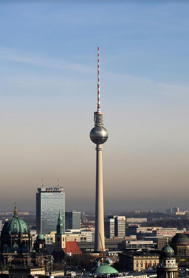 The Berlin TV Tower rises above the city, surrounded by modern buildings and historic churches. A clear sky in the background.