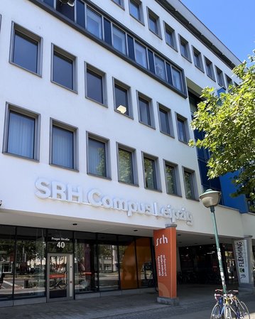 SRH Campus Leipzig mit Eingangsbereich und Schildern. Fahrräder stehen vor dem Gebäude, das moderne Architektur zeigt.