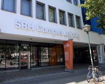 SRH Campus Leipzig with an entrance area and signs. Bicycles are parked in front of the building, which showcases modern architecture.
