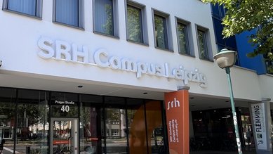 SRH Campus Leipzig mit Eingangsbereich und Schildern. Fahrräder stehen vor dem Gebäude, das moderne Architektur zeigt.