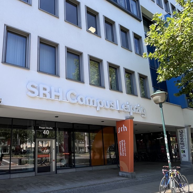 SRH Campus Leipzig with an entrance area and signs. Bicycles are parked in front of the building, which showcases modern architecture.