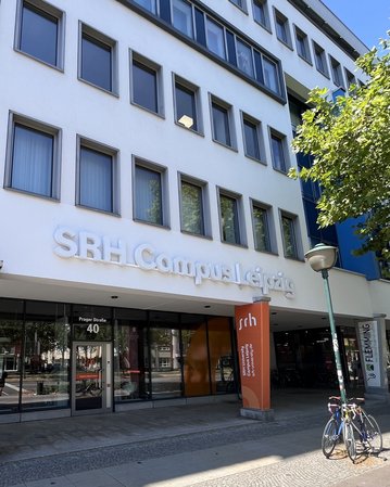 SRH Campus Leipzig with an entrance area and signs. Bicycles are parked in front of the building, which showcases modern architecture.