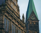 Das historische Rathaus mit aufwendiger Fassade und der markante Turm mit grünem Dach und Uhr im Hintergrund.