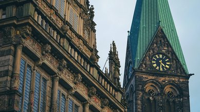 Das historische Rathaus mit aufwendiger Fassade und der markante Turm mit grünem Dach und Uhr im Hintergrund.