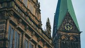 Das historische Rathaus mit aufwendiger Fassade und der markante Turm mit grünem Dach und Uhr im Hintergrund.