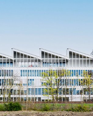 Modern office building with large windows and a distinctive, wave-shaped roof. Surrounded by trees and open landscape.