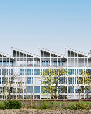 Modernes Bürogebäude mit großen Fenstern und einem markanten, wellenförmigen Dach. Umgeben von Bäumen und einer offenen Landschaft.