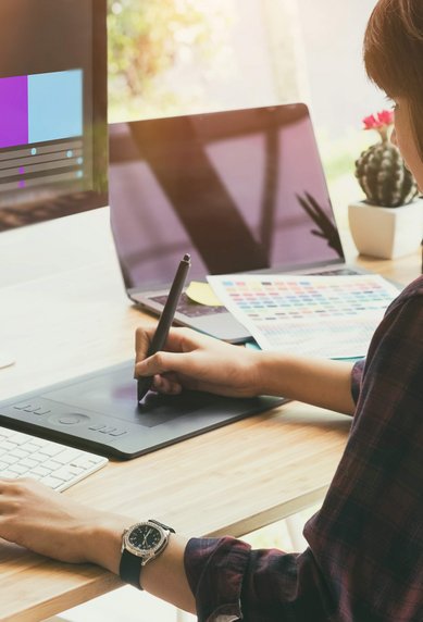 Eine Person arbeitet an einem Grafikdesign-Projekt mit einem Grafiktablett, während ein Computerbildschirm eine Farbpalette zeigt.