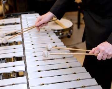 A musician plays with two mallets on a xylophone while focusing on the sheet music.