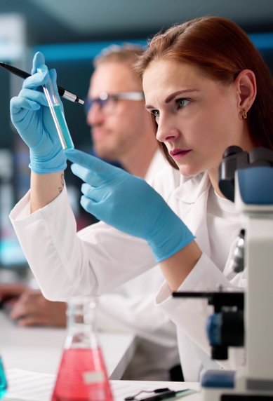 A scientist in a lab is examining a sample with a pipette, while other researchers are working in the background.