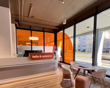 Modern reception desk with the inscription 'hello & welcome,' surrounded by windows and a cozy seating area.