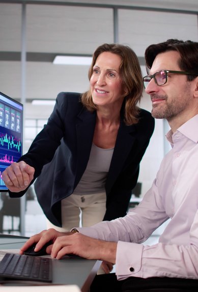 A woman is showing a man and a woman data visualizations and charts on several screens in a modern office.