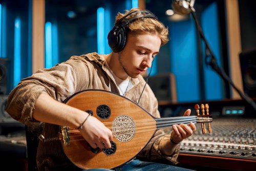 Ein junger Mann spielt eine Oud in einem Tonstudio, während er Kopfhörer trägt. Im Hintergrund sind Mischpult und Studiolichter sichtbar.