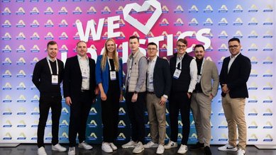 Eine Gruppe von acht Personen steht vor einem bunten Hintergrund mit dem Text "WE ♥ Analytics". Alle tragen legere Kleidung und lächeln.