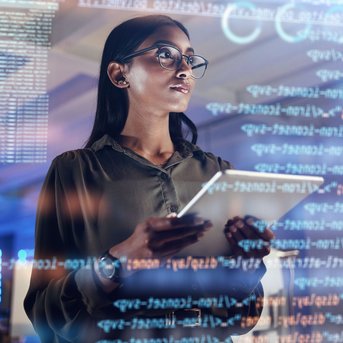 Eine Frau mit Brille hält ein Tablet und betrachtet digitale Daten und Programmiercode auf einem Bildschirm in einem modernen Büro.