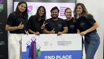 Fünf Personen in schwarzen T-Shirts stehen zusammen und halten ein Schild mit der Aufschrift "2ND PLACE" und dem Thema "Innovative Lösungen für Gesundheit und Wohlbefinden".