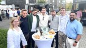 Eine Gruppe von sieben Personen steht um einen Tisch mit Getränken und Snacks, lächelnd und posierend für ein Foto.
